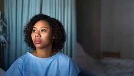 A female patient sits on a hospital bed.